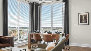 A modern living room with a dining area, large windows with blinds, a ceiling fan, and a view of the cityscape. - 2 King Suites Walk to Broadway & Gulch (Nashville)