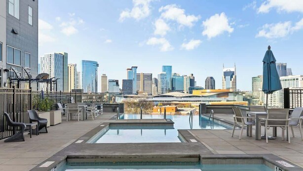 Piscina en la azotea con vistas a la ciudad, sillones de descanso y una sombrilla azul.