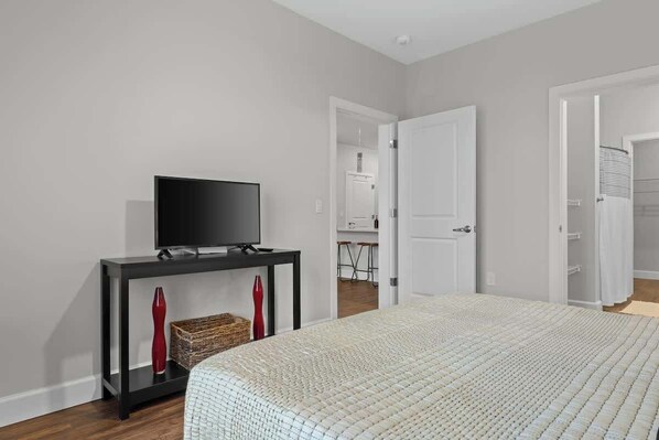 A bedroom with a bed, a TV on a stand, and a door leading to a bathroom.