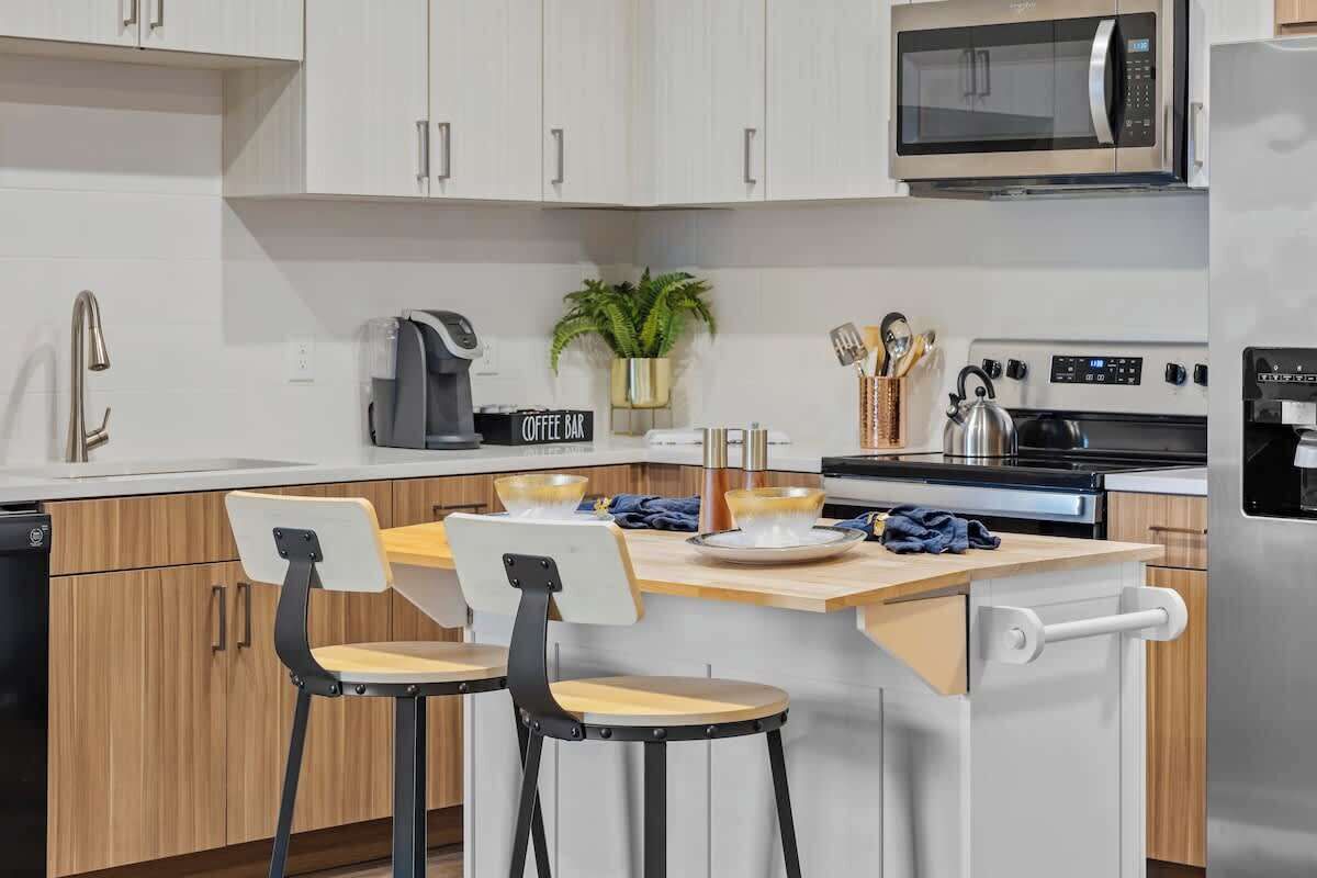 A modern kitchen with white cabinets, a microwave, an oven, and a coffee bar.