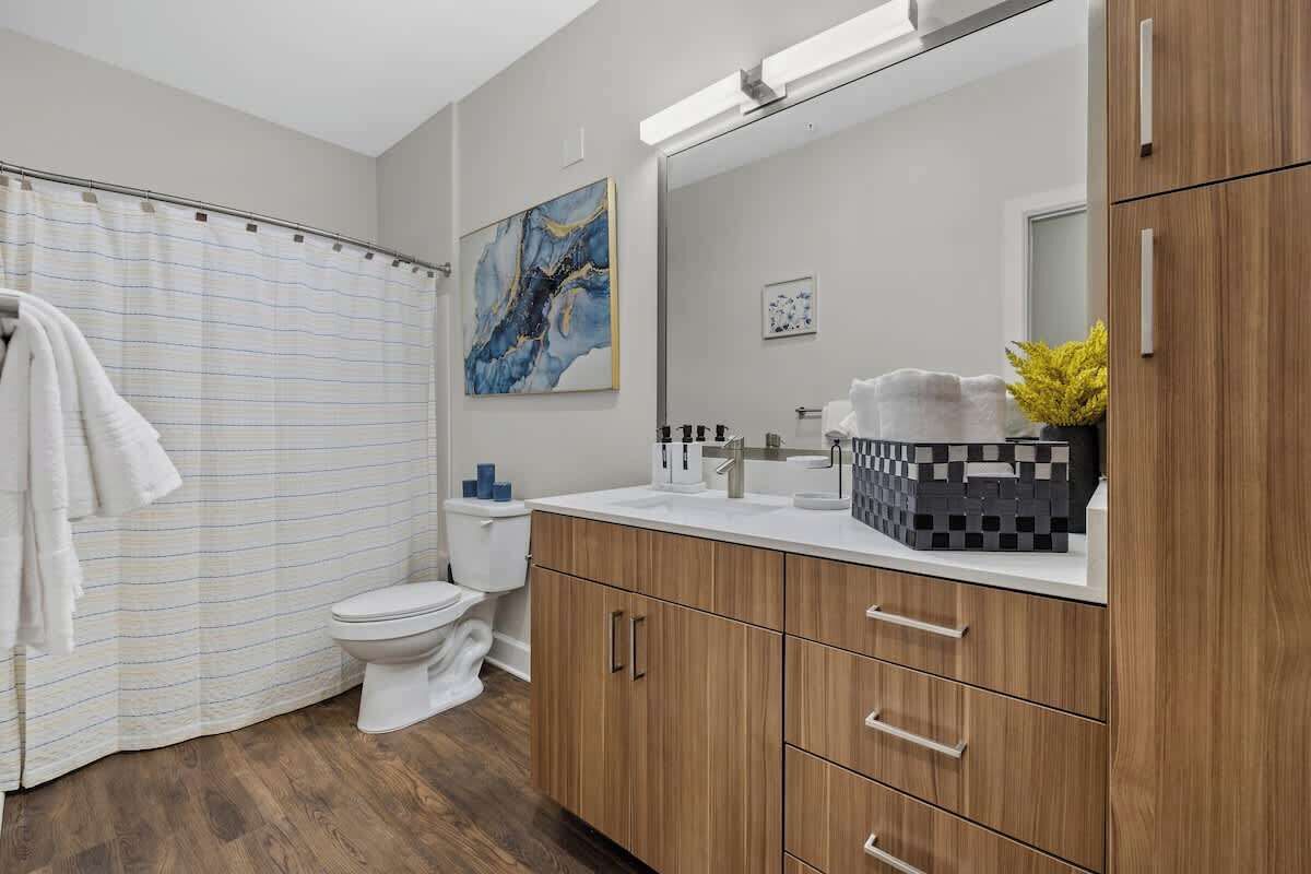 A modern bathroom with a shower curtain, toilet, wooden cabinets, and a large mirror.