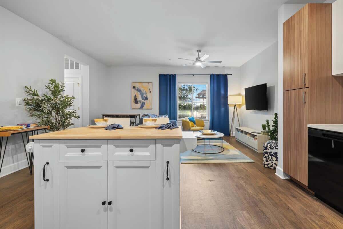 A modern kitchen with white cabinets, a wooden countertop, and a dining area with a yellow sofa and blue curtains.