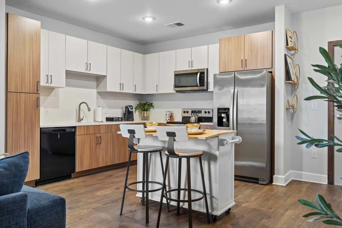 A modern kitchen with white cabinets, stainless steel appliances, and a bar area with stools.