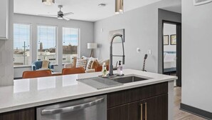 Een moderne keuken met een groot eiland, donkere kasten en een stadszicht door grote ramen.