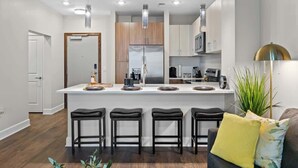 A modern kitchen with a central island, bar stools, and a microwave. - Luxe Gulch 1BR near Broadway | Sleeps 6 (Nashville)