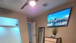 Een slaapkamer met een bed, een dressoir, een aan de muur bevestigde televisie en een plafondventilator.