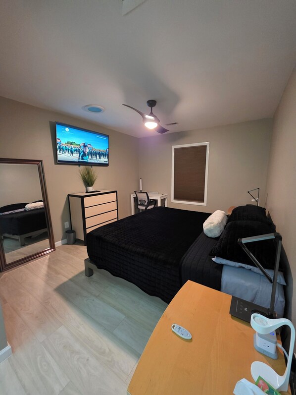 A modern bedroom with a bed, a desk, a chair, a TV, and a ceiling fan.