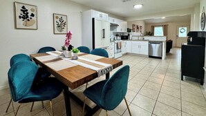 A modern kitchen with white cabinets, a stainless steel refrigerator, and a dining area with a wooden table and teal chairs. - Swim, Hike, Explore & Relax just minutes from lakes-beaches, nature & Ft. Worth! (Azle)