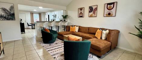 A spacious living area with a brown sofa, green armchairs, and a patterned rug. A ceiling fan and recessed lighting are visible.