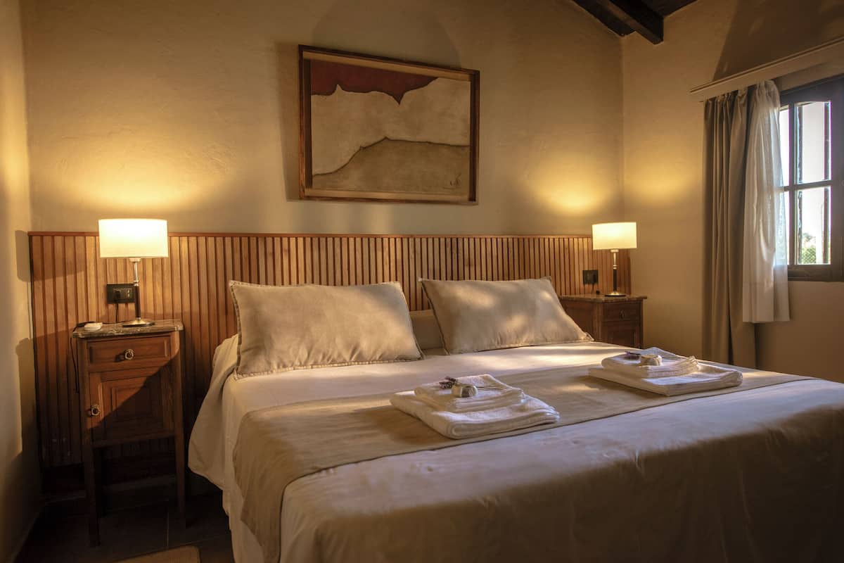Habitación de hotel con una cama grande, dos mesitas de noche con lámparas, un cabecero de madera y un cuadro en la pared.