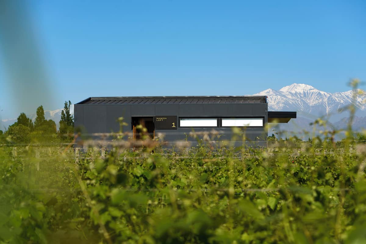 Un edificio moderno con techo plano y ventanas amplias, con montañas nevadas al fondo.