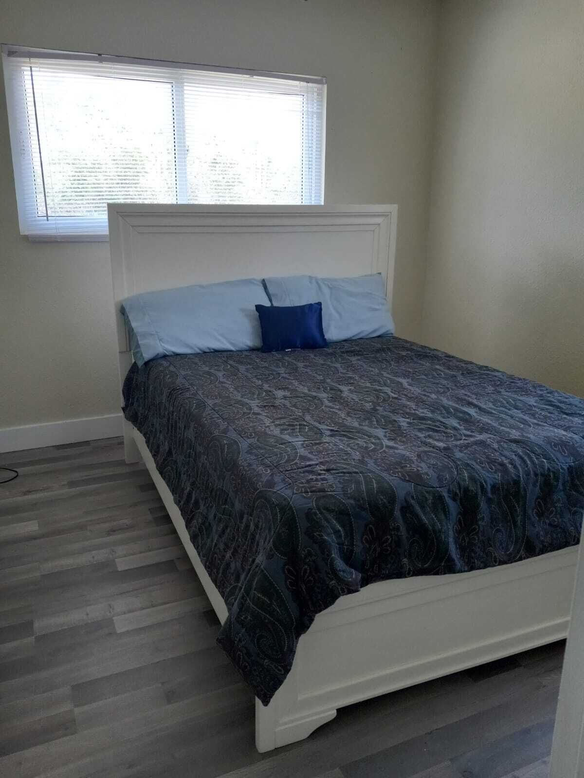 A bedroom with a bed, a window, and a wooden floor.
