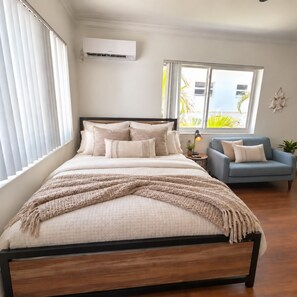 A bedroom with a bed, a chair, a nightstand, and a window with blinds.