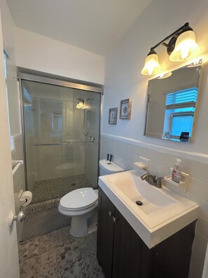 A modern bathroom with a glass-enclosed shower, a toilet, a sink with a mirror, and a small shelf with toiletries.