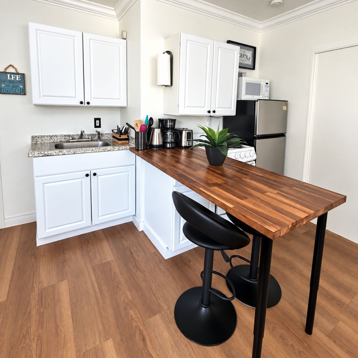 Una cocina con armarios blancos, una encimera de madera, un taburete negro y un refrigerador de acero inoxidable.