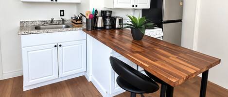 Una cocina con armarios blancos, una encimera de madera, un taburete negro y un refrigerador de acero inoxidable.