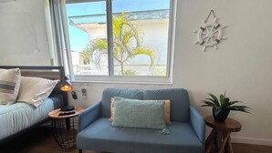A room with a sofa, a small table with a lamp, a potted plant, and a view of the beach through a window. - Salt + Sun Studio, feet from Hollywood Beach (Hollywood)