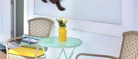 A room with two wicker chairs, a small glass table, and a yellow vase with flowers.