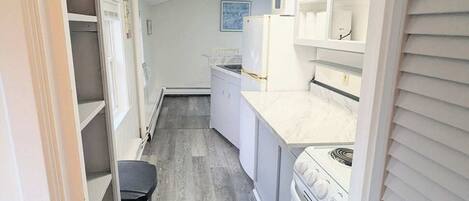 A narrow kitchen with white cabinets, a stove, and a microwave.