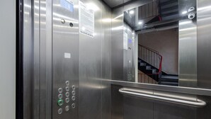 An elevator interior with metallic walls, a handrail, and a control panel with buttons.