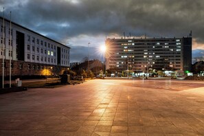 Tilava kaupunkiaukio, jonka yhteydessä on suuri, useita kerroksia sisältävä rakennus, jossa on tasakatto. Aukion ympärillä on kivetty alue, jossa on katuvaloja ja muutamia puita.