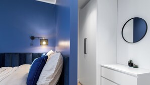 A bedroom with a bed, a nightstand, a wall-mounted lamp, and a bedside table.
