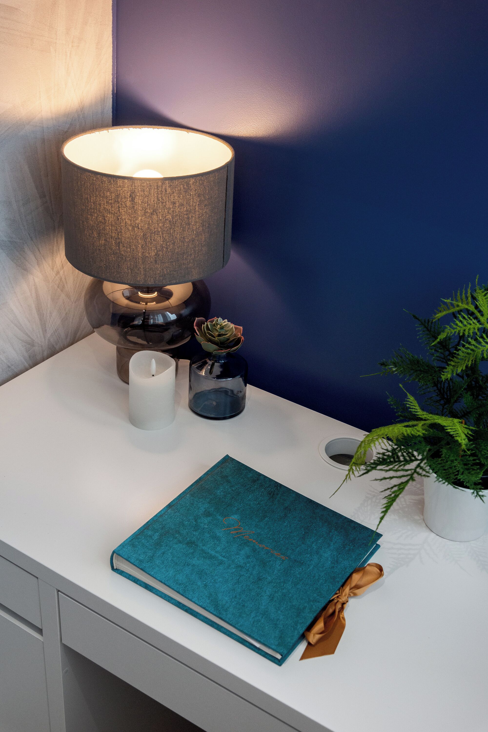 Et natbord med en turkis bog, et lys, en lampe og en lille plante.