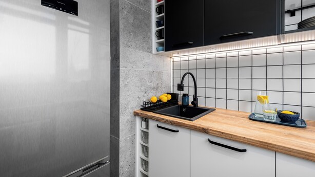 A modern kitchen with a stainless steel refrigerator, a black sink, and a wooden countertop.