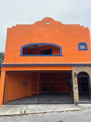 A two-story building with a bright orange facade, a large garage with a metal gate, and a small window on the upper floor. - Casa Colonial en Pueblo Mágico by Adhoc (Santiago)