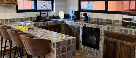 A modern kitchen with a central island, bar stools, a built-in oven, and a backsplash with patterned tiles.