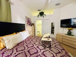 A bedroom with a bed, a TV, a dresser, and a door leading to another room.
