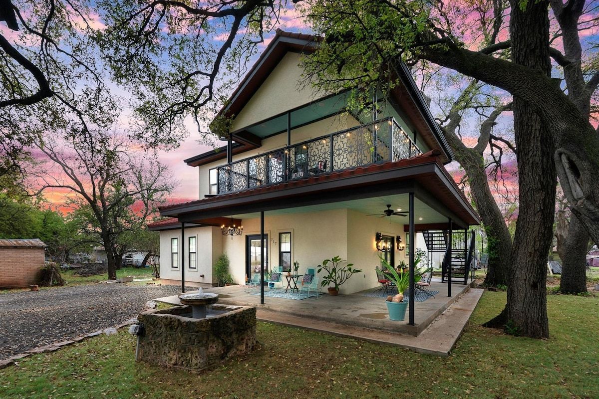 Ein zweistöckiges Haus mit einem Balkon, einer überdachten Terrasse und einem Kamin aus Stein.