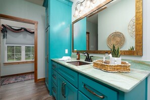 A bathroom with a teal vanity, a sink, a mirror, and a window with a view.
