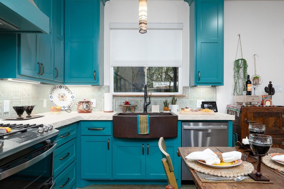 A kitchen with teal cabinets, a window above the sink, and a dining area with a table set for two.