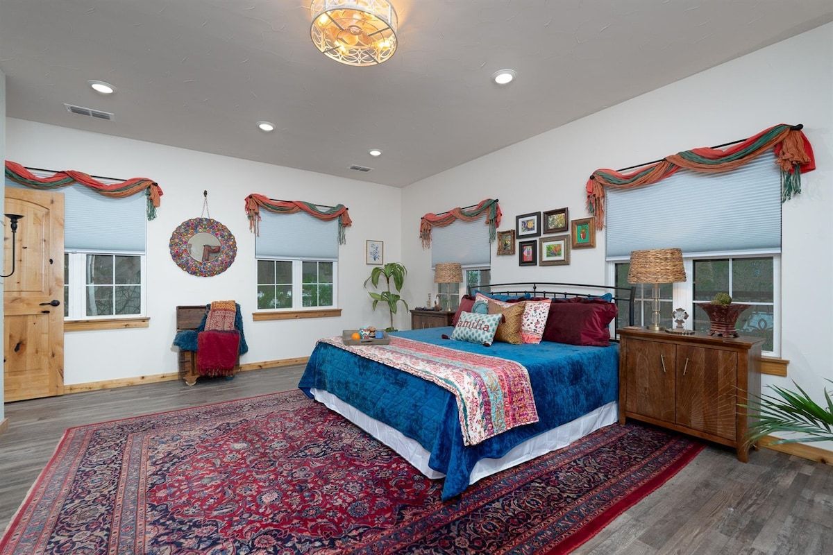 A bedroom with a large bed, a wooden wardrobe, a red patterned rug, and a wall-mounted mirror.