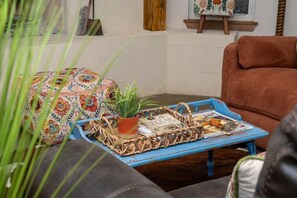 A cozy living area with a patterned ottoman, a blue woven tray with books and a plant, and a brown sofa.