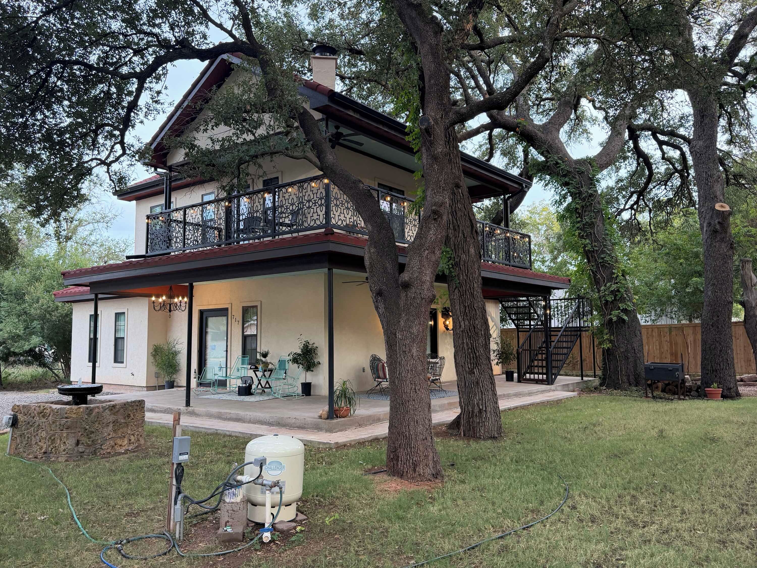 A two-story house with a balcony, surrounded by large trees.