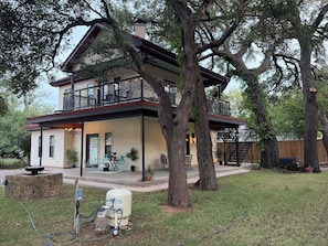 Una casa de dues plantes amb un balcó, envoltada d'arbres grans.
