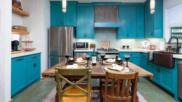 A kitchen with teal cabinets, stainless steel appliances, and a wooden dining table set for four.
