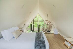 Ein Schlafzimmer mit einem großen Bett, einem Hängesessel und Blick auf Grün durch ein Fenster.