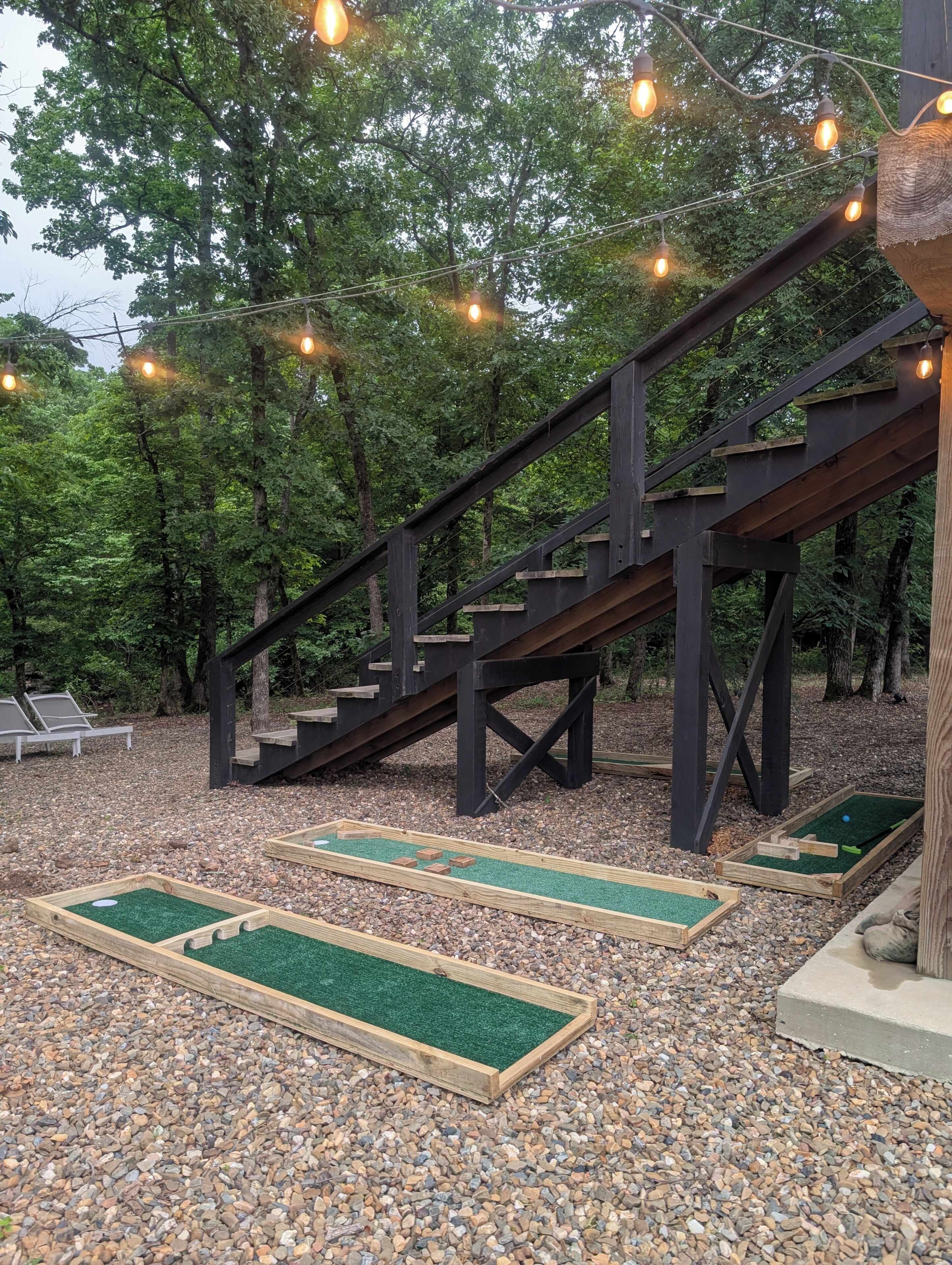 A wooden staircase with a wooden deck, surrounded by trees and gravel.