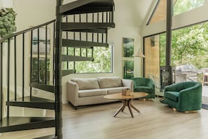 Ein modernes Interieur mit einer Treppe, einem Sofa, einem runden Tisch und grünen Sesseln.