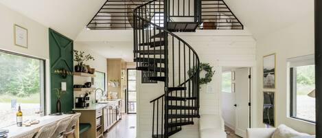 Un interior moderno con una escalera espiral, una zona de comedor con taburetes de bar, un sofá y una chimenea.