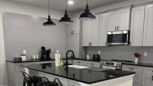 Una cocina moderna con una isla central, taburetes de bar, electrodomésticos de acero inoxidable e iluminación colgante.