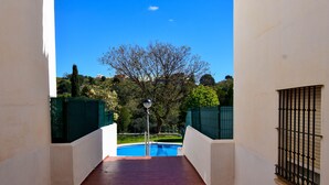 Une vue depuis un balcon donnant sur une piscine, avec un arbre et un lampadaire en arrière-plan.