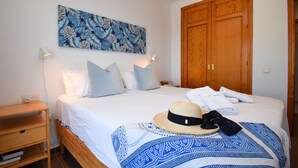 Un lit bien fait, recouvert d’une couvre-lit à motifs bleus, une table de chevet en bois, une lampe fixée au mur et une grande armoire en bois.