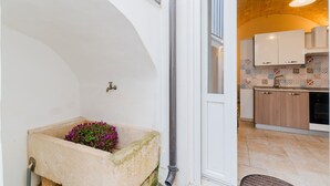 Un lavamanos de piedra con flores, una puerta blanca y una cocina con armarios de madera y un salpicadero de azulejos.