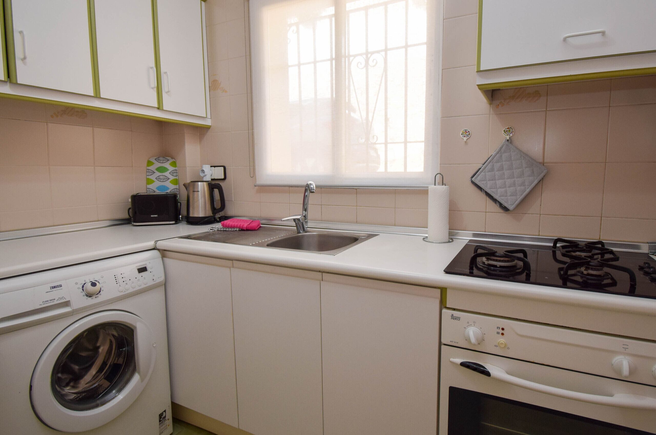 A compact kitchen with a washing machine, a sink, a stove, and a window.