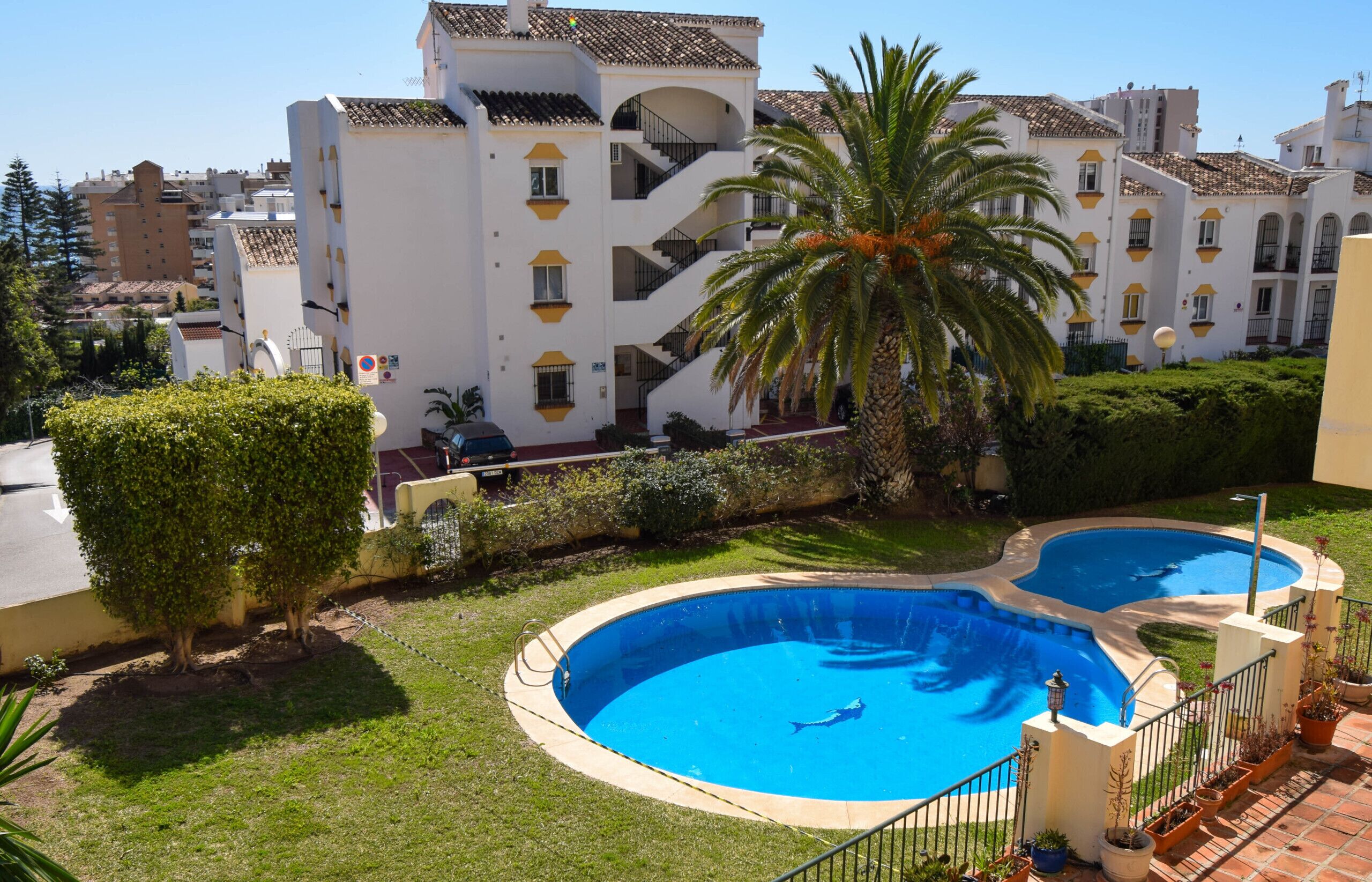 A residential building with a swimming pool, palm trees, and a well-maintained lawn.