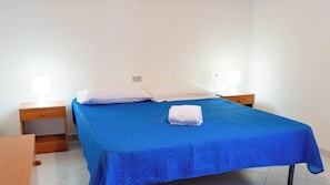 Un lit simple avec une couvre-lit bleue, deux tables de chevet avec des lampes et une serviette blanche pliée posée sur le lit.